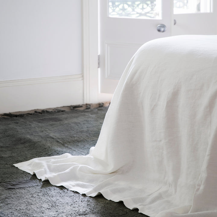 A bed is dressed with a White Flat Sheet which drapes on the floor.