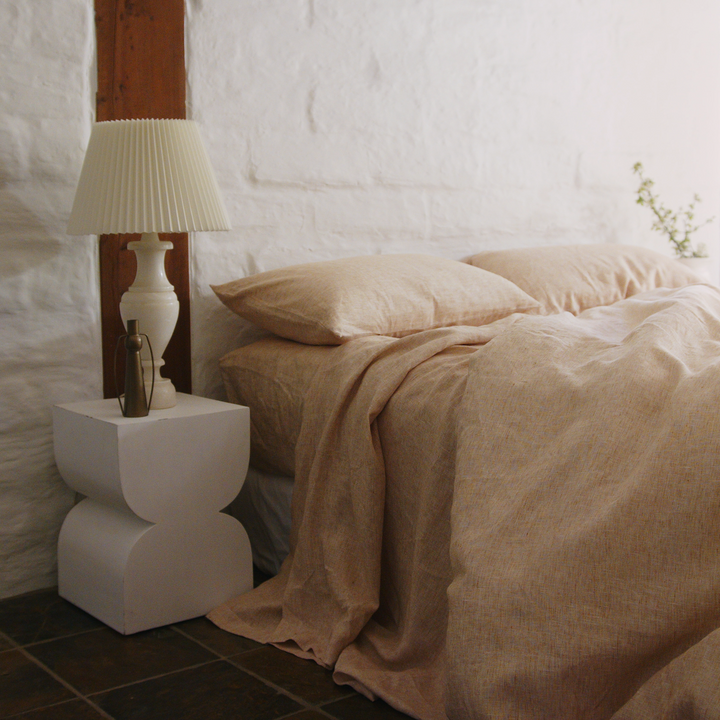 A bed dressed in Cinnamon and White bed linen, styled with a  modern bedside table and plant