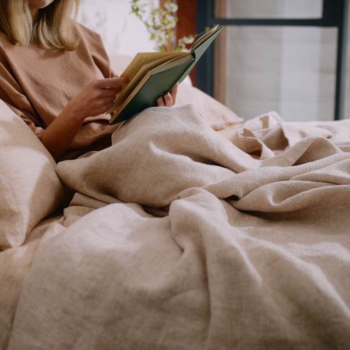 A woman reading a book on a bed dressed in pure linen bedding in Cinnamon