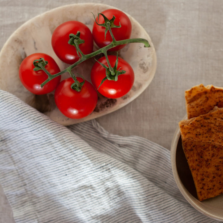 A close up of a Linen Table Napkin in Pinstripe, placed next to a bowl of tomatoes and a bowl of crackers.