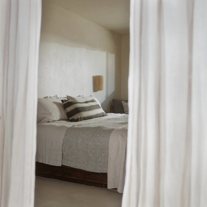 A bed dressed in Natural bedlinen with a Heavy Chambray Bedcover in Black and a Mira Enzo Lumbar Cushion.