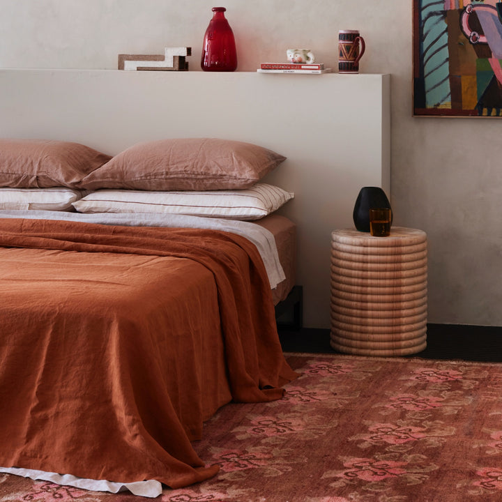 A bed dressed in Cedar, Smoke Gray, Fawn and Cedar Stripe bed linen, styled with modern artwork and a wooden bedside table